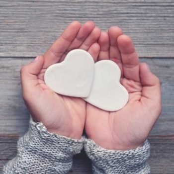 Woman holding two white love hearts. A woman is holding them in her hands. There is a rustic wood table underneath her hands. Valentines day or anniversary concept. Copy space.